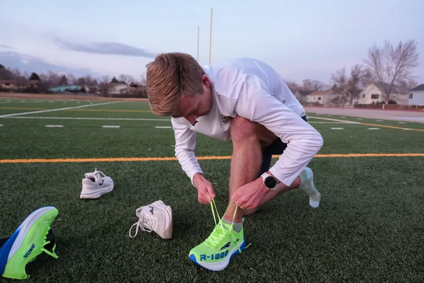 An Apex Elite athlete lacing up racing shoes on the field at dusk